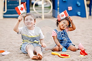 Caucasian boy and latin hispanic baby girl holding waving Canadian flags.