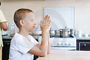 Caucasian boy prays at home at the table before eating. Stay home and pray