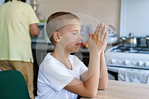 Caucasian boy prays at home at table before eating. Stay home and pray to god.