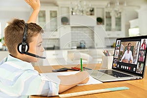 Caucasian boy raising hand for video call, with smiling diverse elementary school pupils on screen