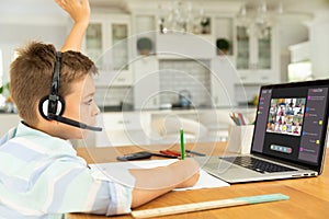 Caucasian boy raising hand for video call, with smiling diverse elementary school pupils on screen