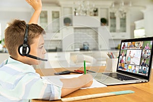 Caucasian boy raising hand for video call, with smiling diverse elementary school pupils on screen