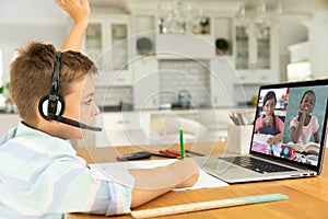 Caucasian boy raising hand for video call, with smiling diverse elementary school pupils on screen