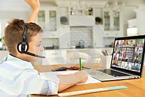 Caucasian boy raising hand for video call, with smiling diverse elementary school pupils on screen