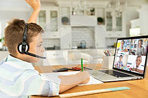 Caucasian boy raising hand for video call, with smiling diverse elementary school pupils on screen