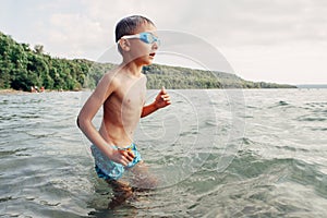 Caucasian boy swimming in lake river with underwater goggles. Child diving in water on a beach. Authentic real lifestyle happy