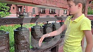 Caucasian boy touching, rotating nepalese traditional metal prayer wheels with mantra Om Mani Padme Hum, that means O