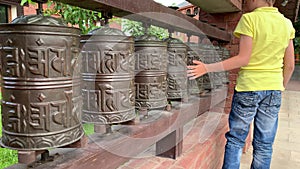 Caucasian boy touching, rotating nepalese traditional metal prayer wheels with mantra Om Mani Padme Hum, that means O