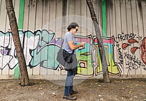 Caucasian boy uses his mobile phone next to a painted wall on a city street