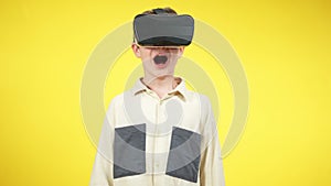 Caucasian boy in VR headset screaming at yellow background. Middle shot of excited kid using augmented reality for