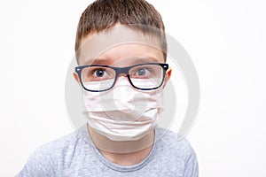A caucasian boy wearing glasses in white face surgical mask on white background, protection against flu and virus infection