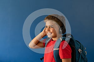 Caucasian boy wearing headphones with backpack standing on blue background, copy space