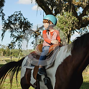 Caucasian boy wearing helmet and riding horse in greenery field