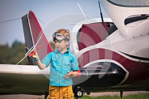 Caucasian boy in yellow shorts, a blue shirt and in aviation points holds the toy plane in hand and h