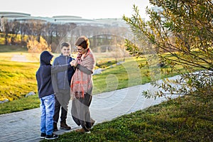 Caucasian boys in warm casual clothes give mom flower in autumn park in selective focus