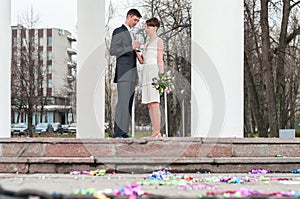 Caucasian bridal pair cheers and clink wine glasses with champagne, bride and groom are between white columns outdoor