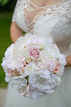 Caucasian bride wearing an elegant white dress while holding a large wedding bouquet of artificial roses and peonies