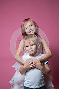 Caucasian brother and sister ,hugging on camera on pink background studio shot.