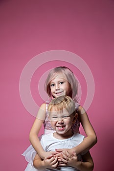 Caucasian brother and sister ,hugging on camera on pink background studio shot.