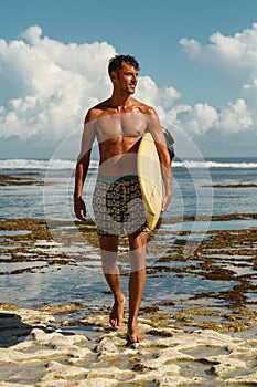 Caucasian brunette with tan skin male surfer coming  out of the ocean