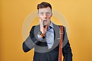 Caucasian business man over yellow background afraid and shocked, surprise and amazed expression with hands on face