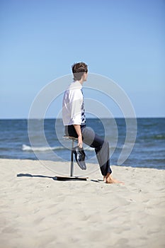 Caucasian business man sitting on pneumatic stool on the beach