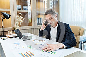 Caucasian business manager using phone to call customer while analyzing the sales report from marketing team for business income
