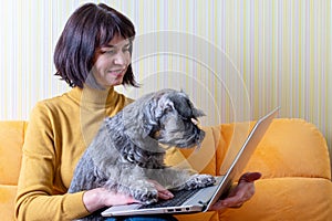 Caucasian business woman and her pet dog typing on laptop at home office. Middle aged woman working on laptop