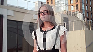 Caucasian business woman in white shirt and glasses walking down the street near a modern office building.