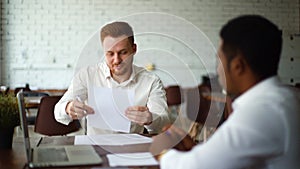 Caucasian businessman and African-American business man signing contract sitting at office desk.