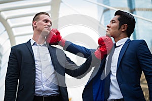 Caucasian businessman and asian businessman with red boxing gloves fighting by uppercut to chin. concept of business competition.