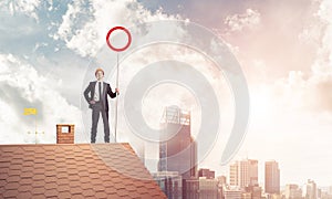 Caucasian businessman on brick house roof showing stop road sign