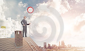 Caucasian businessman on brick house roof showing stop road sign