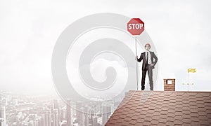 Caucasian businessman on brick house roof showing stop road sign