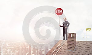 Caucasian businessman on brick house roof showing stop road sign