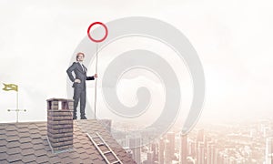 Caucasian businessman on brick house roof showing stop road sign