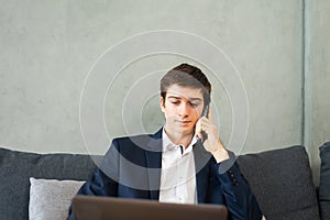 caucasian businessman calling by mobile phone, working on computer, wear suit, sitting, looking at laptop, space at wall