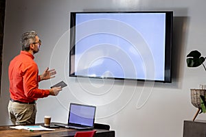 Caucasian businessman holding a digital tablet having a video call on tv with copy space at office