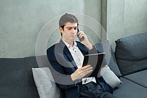 caucasian businessman seriously calling by mobile phone, working and looking at tablet, wear suit, sitting, copy space at