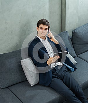caucasian businessman seriously calling by mobile phone, working with tablet, wear suit, sitting. Young man work business with