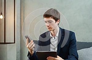 caucasian businessman seriously working and looking to tablet and mobile phone, wear suit, sitting, light and space at background