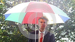 Caucasian businessman sheltering under a colourful umbrella