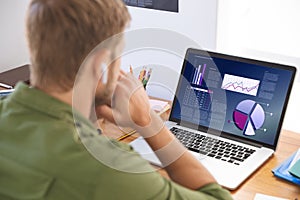 Caucasian businessman sitting at desk using laptop with graph and statistical data on screen photo