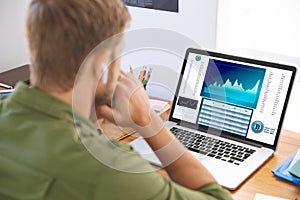 Caucasian businessman sitting at desk using laptop with statistical data on screen photo