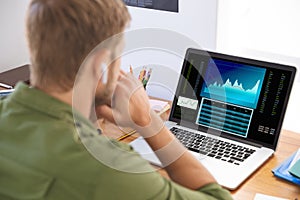 Caucasian businessman sitting at desk, using laptop with statistical data on screen photo