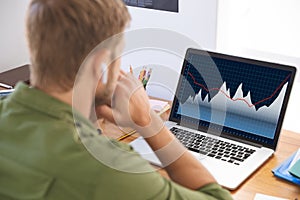 Caucasian businessman sitting at desk, using laptop with statistical data on screen photo