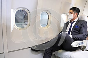Caucasian businessman travels in formal wear with facial mask sitting comfortably in the aircraft with business class seat