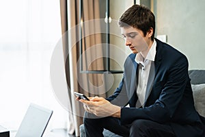 caucasian businessman working with mobile phone, wear suit, sit on sofa, working with laptop. Young man work business with home