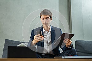 caucasian businessman working with tablet and mobile phone, wear suit, sitting, looking at mobile phone, computer or laptop on