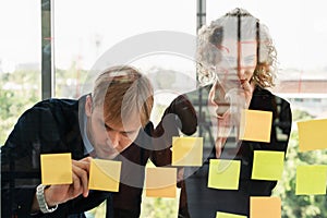 Caucasian businesspeople with glass board and post it note having brainstorming in workplace